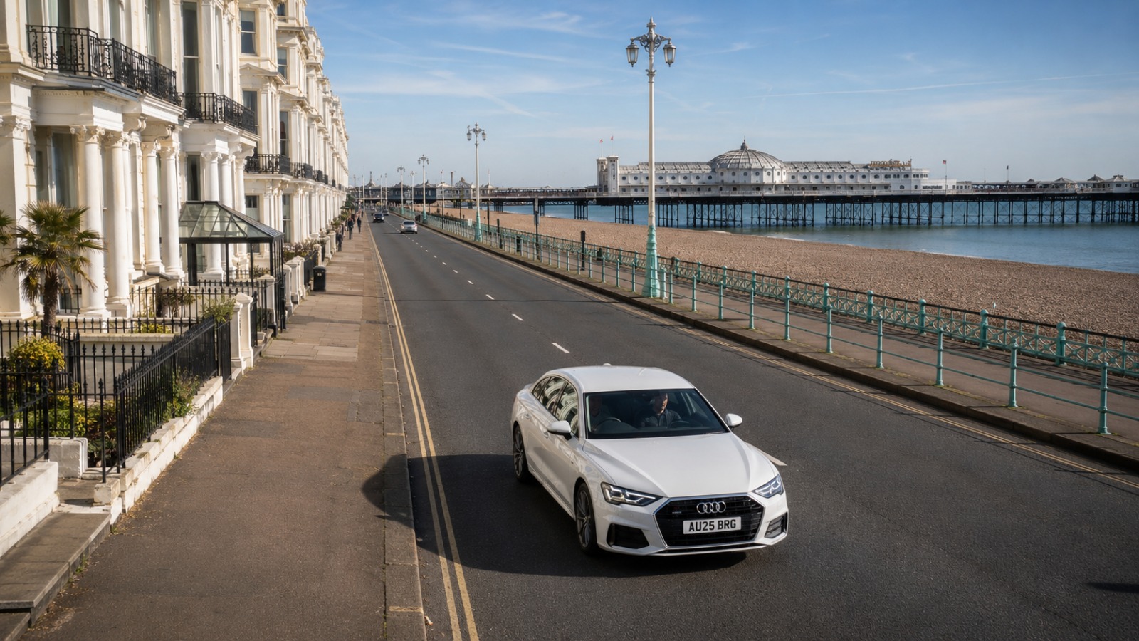 White Audi A6 Saloon Brighton to Gatwick airport taxi on Kings Road seafront at early morning with the pier in the distance.