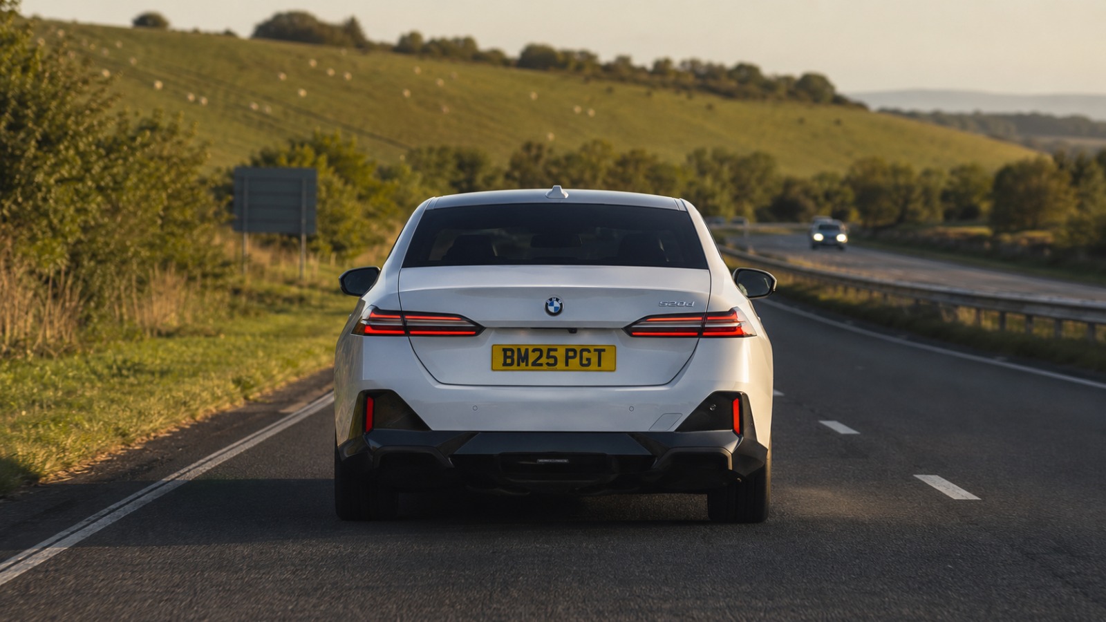 White BMW 5 Series Saloon Portsmouth to Gatwick airport taxi on the A27 through the South Downs in late afternoon light.