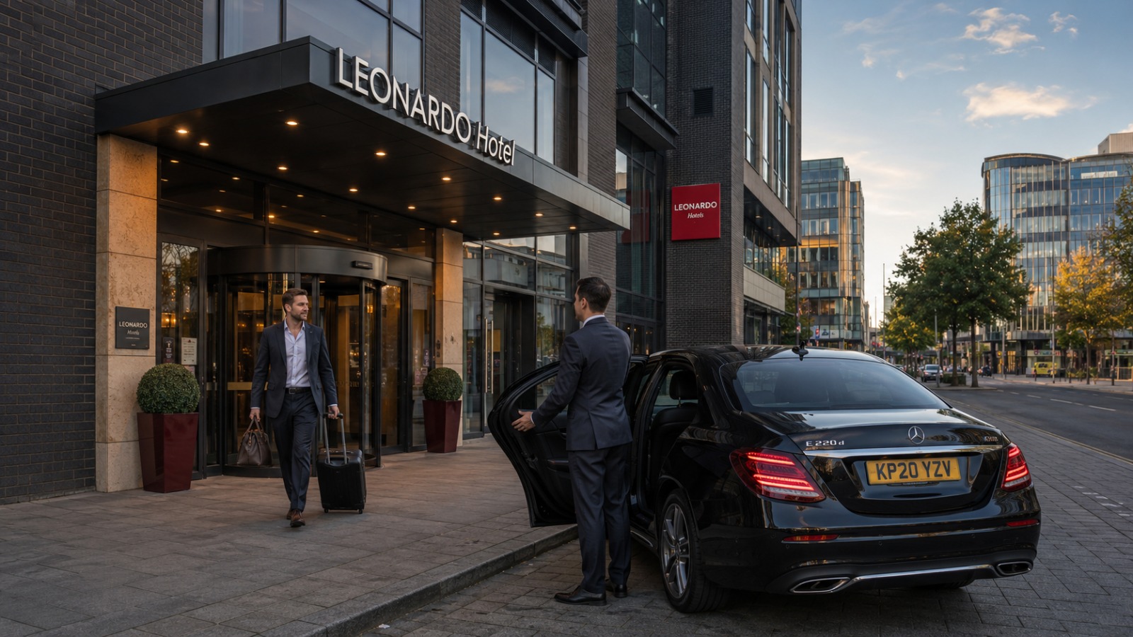 Black executive Mercedes E-Class parked outside a modern Southampton city centre hotel with a business traveller boarding.